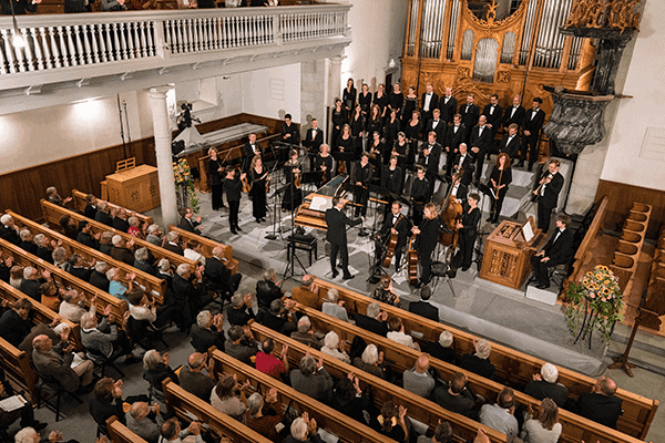 Ein Orchester und ein Chor treten in einer Kirche auf, während das Publikum applaudiert.